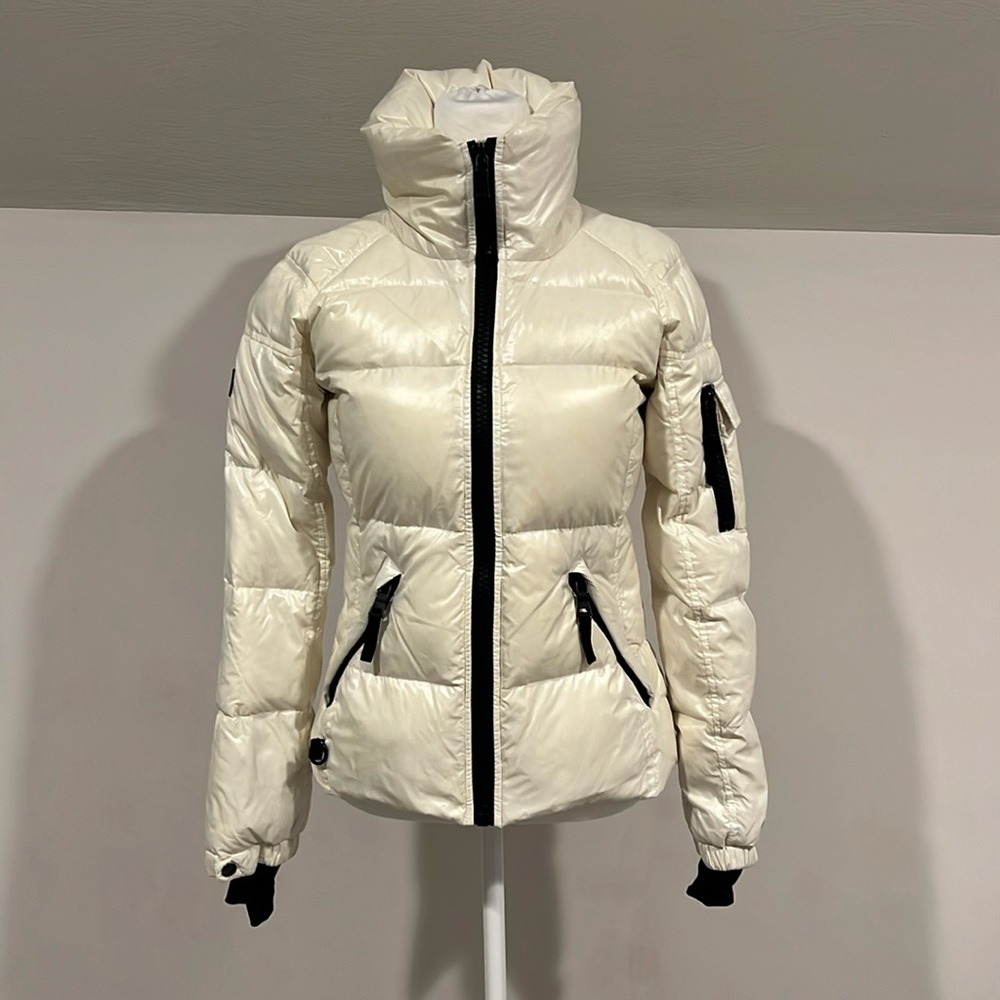 SAM winter coat . Shiny, cream colored  off set with black trim .